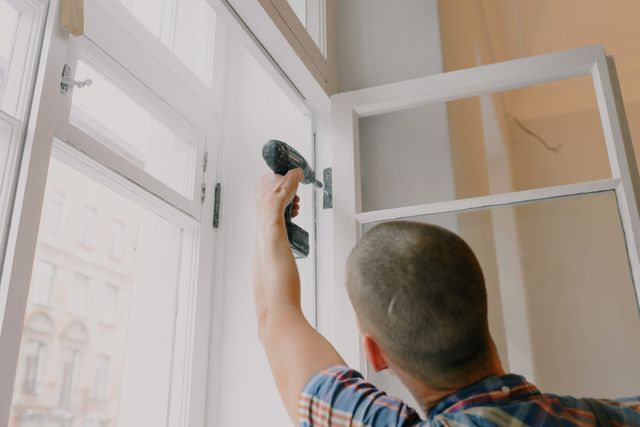 a person fixing a window hinge with a power drill